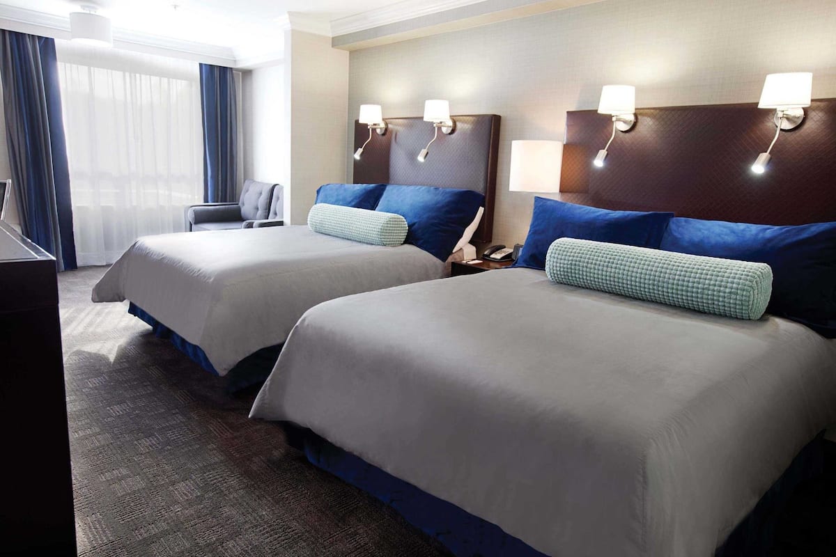 A hotel room with two beds, a desk, a chair, and a large window with curtains.