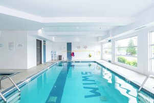 Una amplia piscina cubierta con agua cristalina y azul, rodeada de paredes blancas y grandes ventanales.