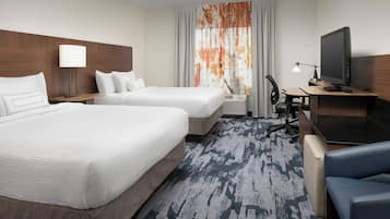 A hotel room with two beds, a desk with a computer, a TV, and a window with curtains.