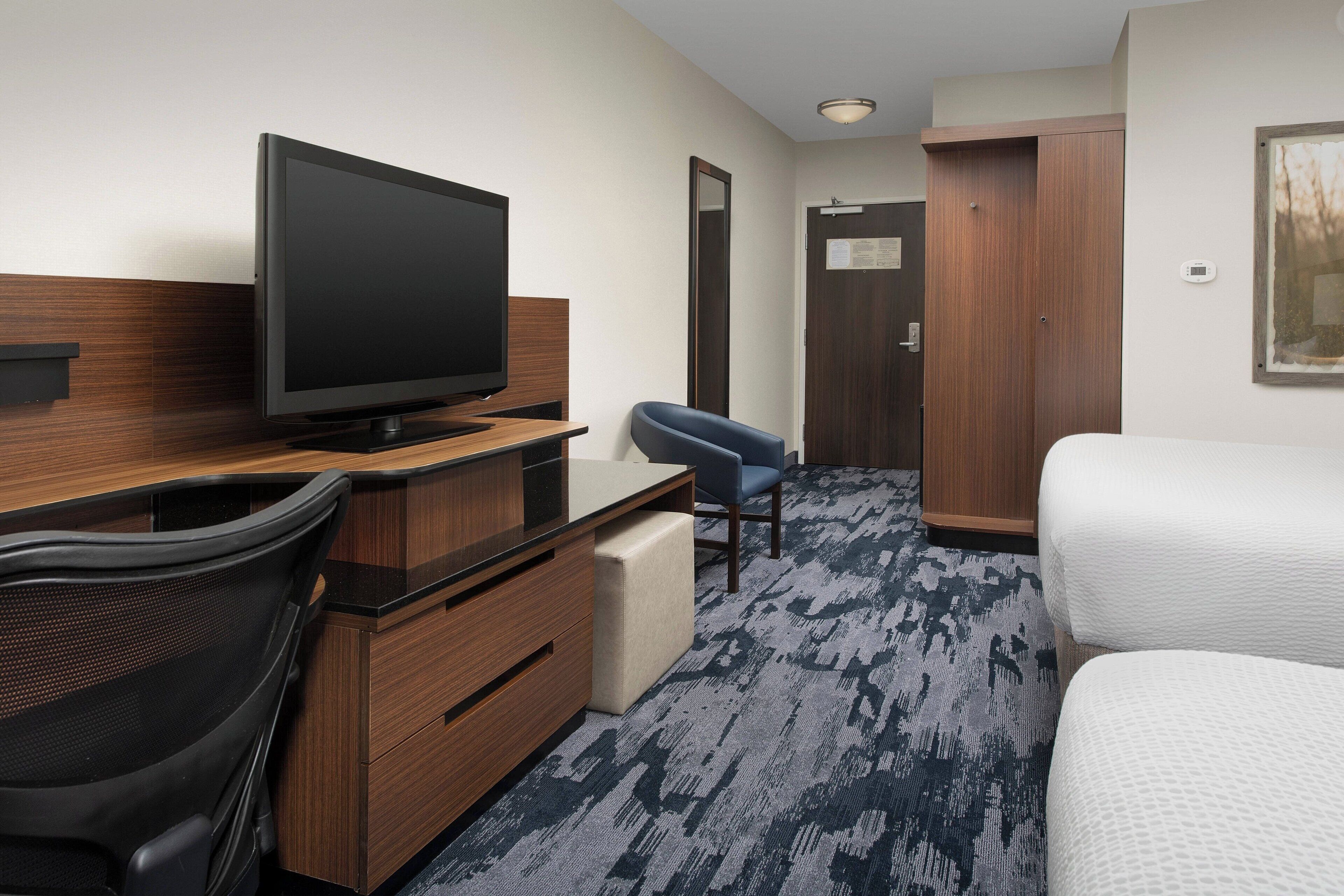 Une chambre d’hôtel équipée d’une télévision à écran plat, d’un bureau avec une chaise, d’un lit et d’une armoire.