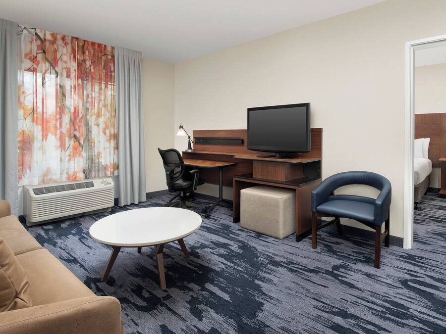 Et hotelværelse med sofa, rundt bord, fjernsyn, skrivebord og stol.