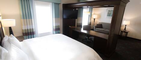 Una habitación de hotel con una cama grande, un escritorio, una silla, un televisor y dos lámparas.