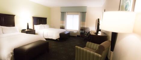 A hotel room with two beds, a chair, a desk, a lamp, and a window with curtains.