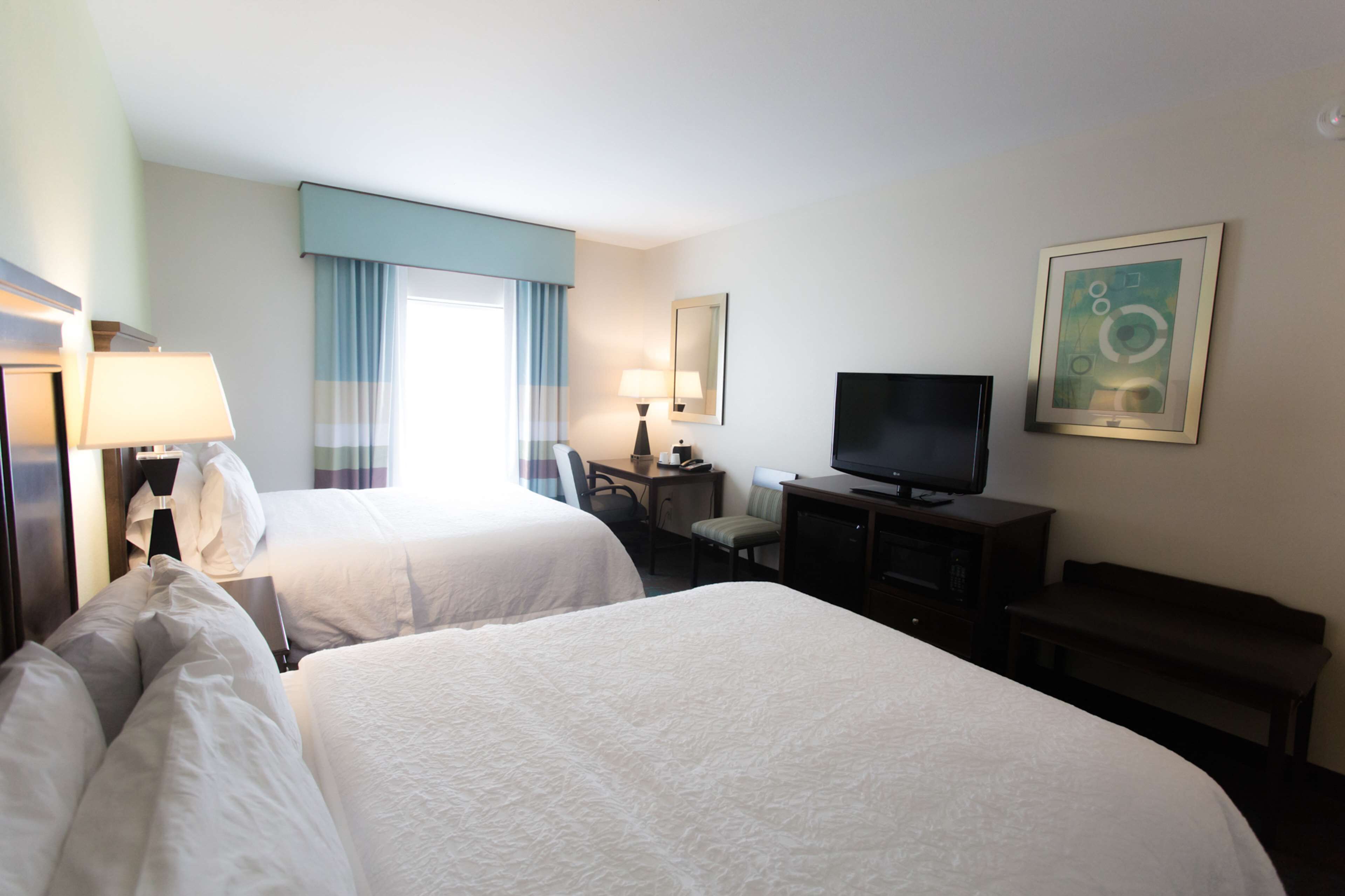Une chambre d’hôtel avec deux lits, un bureau, une télévision et un banc.