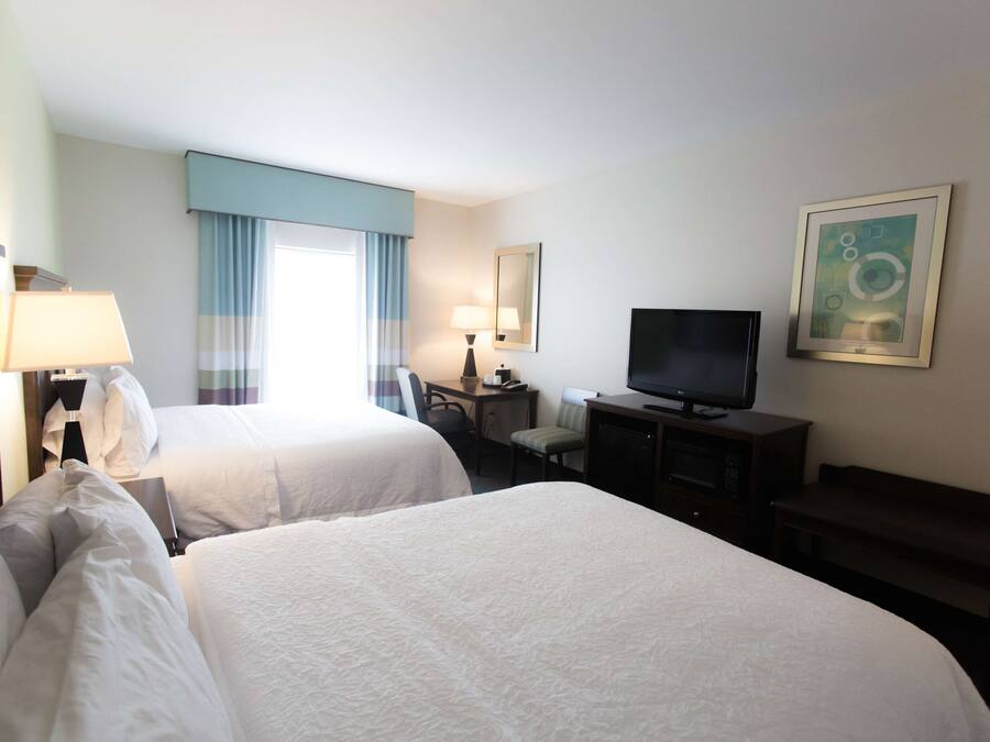 Une chambre d’hôtel avec deux lits, un bureau, une télévision et un banc.