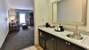 A hotel room with a kitchenette, a large mirror, a sofa, and a dining area with a table and chairs.