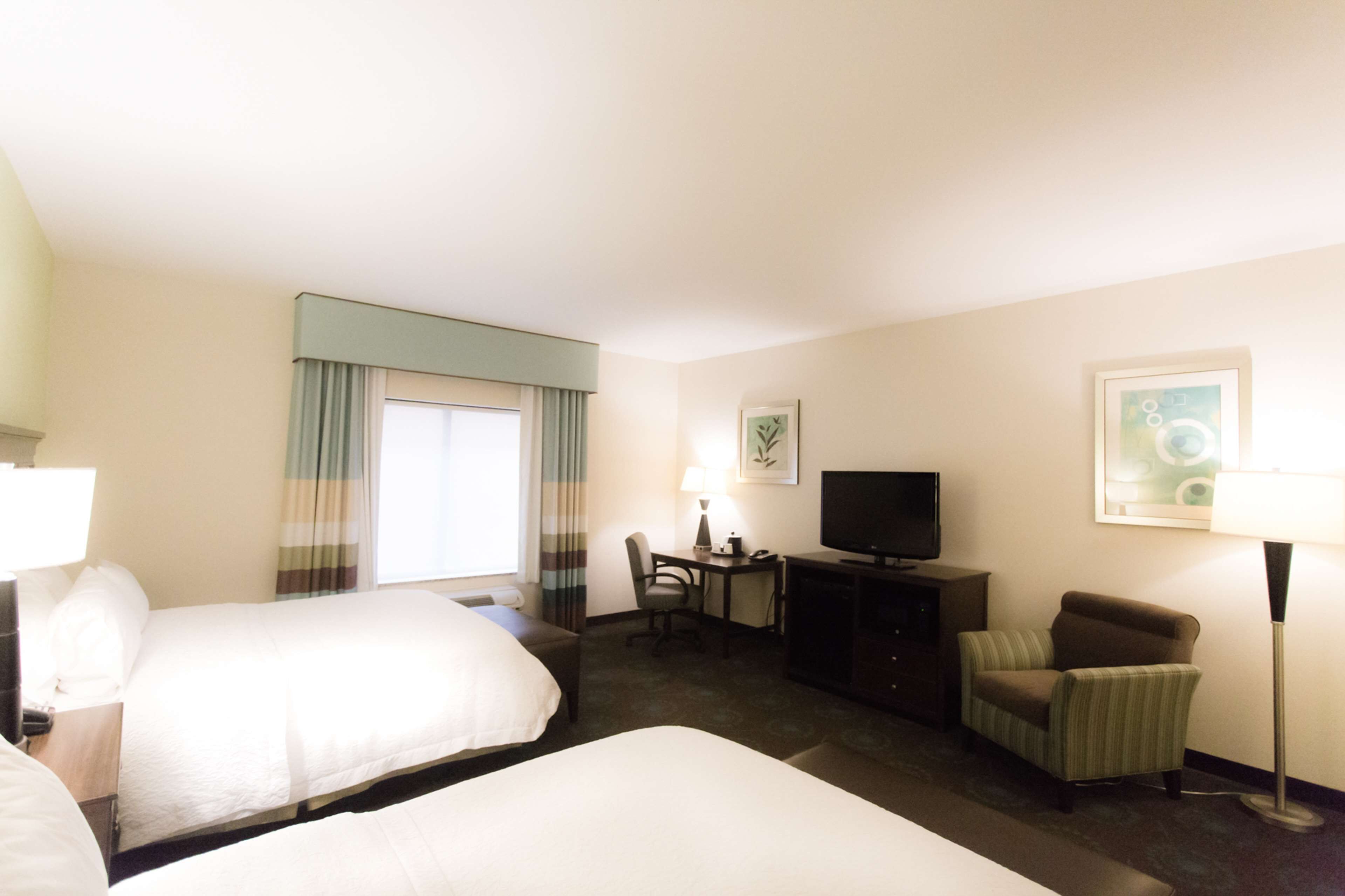 A hotel room with two beds, a desk, a television, a chair, and a lamp.