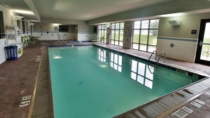 An indoor swimming pool with clear water, a tiled deck, and a view of the outdoors through large windows.