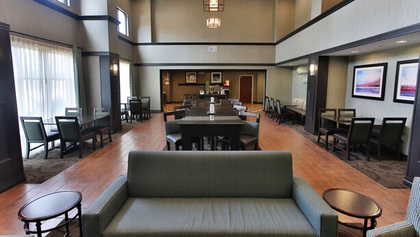 A spacious hotel lobby with a central seating area, multiple dining tables, and a large sofa.