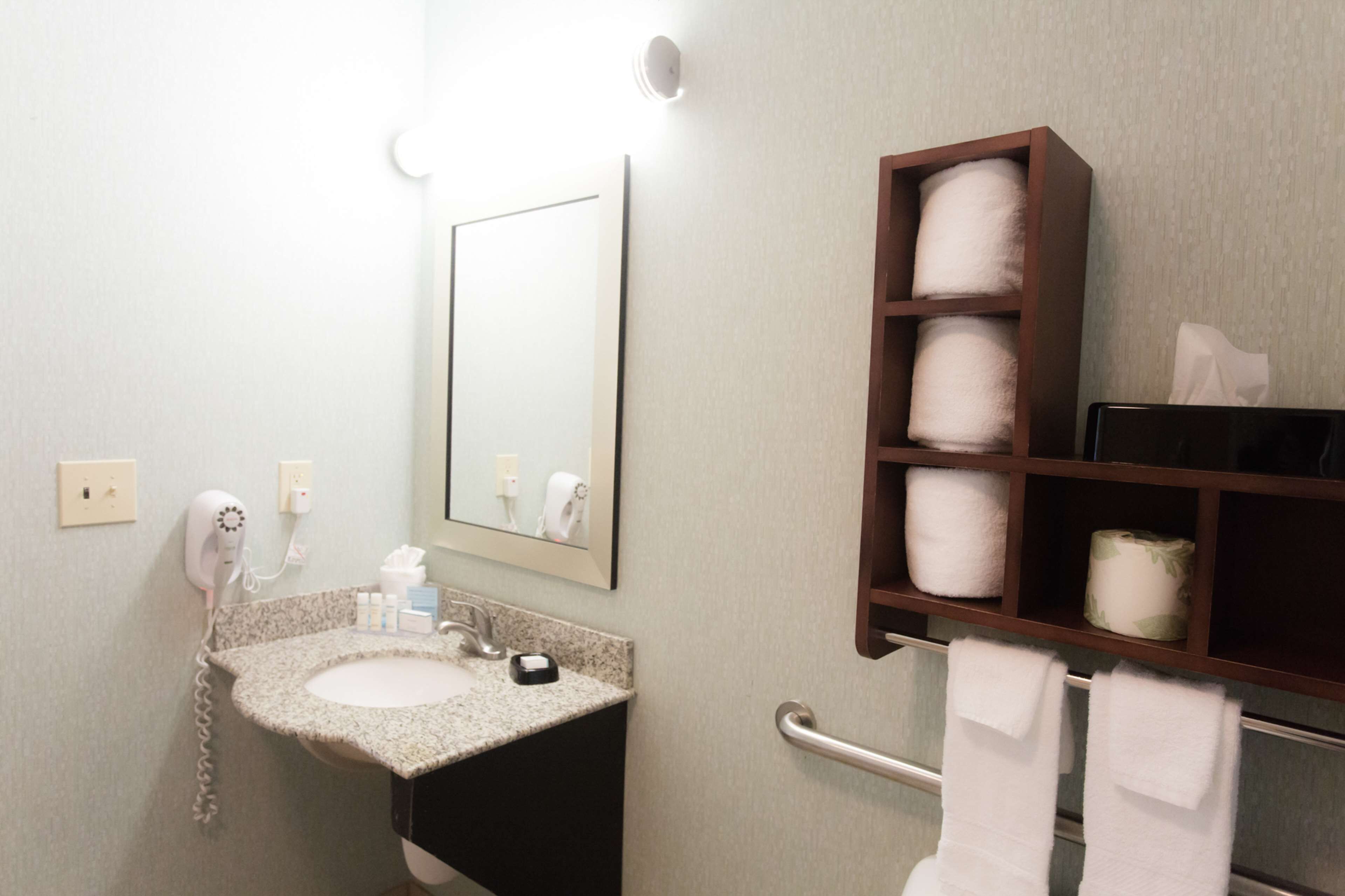 Une salle de bain équipée d’un lavabo, d’un sèche-cheveux, d’un miroir et d’une étagère avec des serviettes.