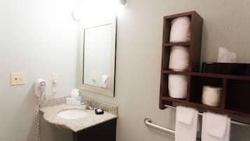 A bathroom with a sink, a hairdryer, a mirror, and a shelf with towels.