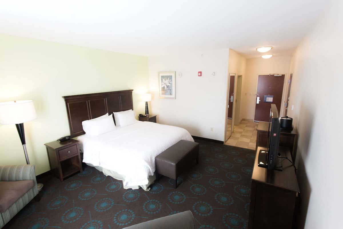 Quarto de hotel com cama, mesas de cabeceira, um banco, escrivaninha com computador e espelho.