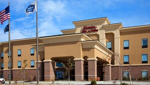 A Hampton Inn & Suites hotel with a brick facade, multiple windows, and a clear blue sky.