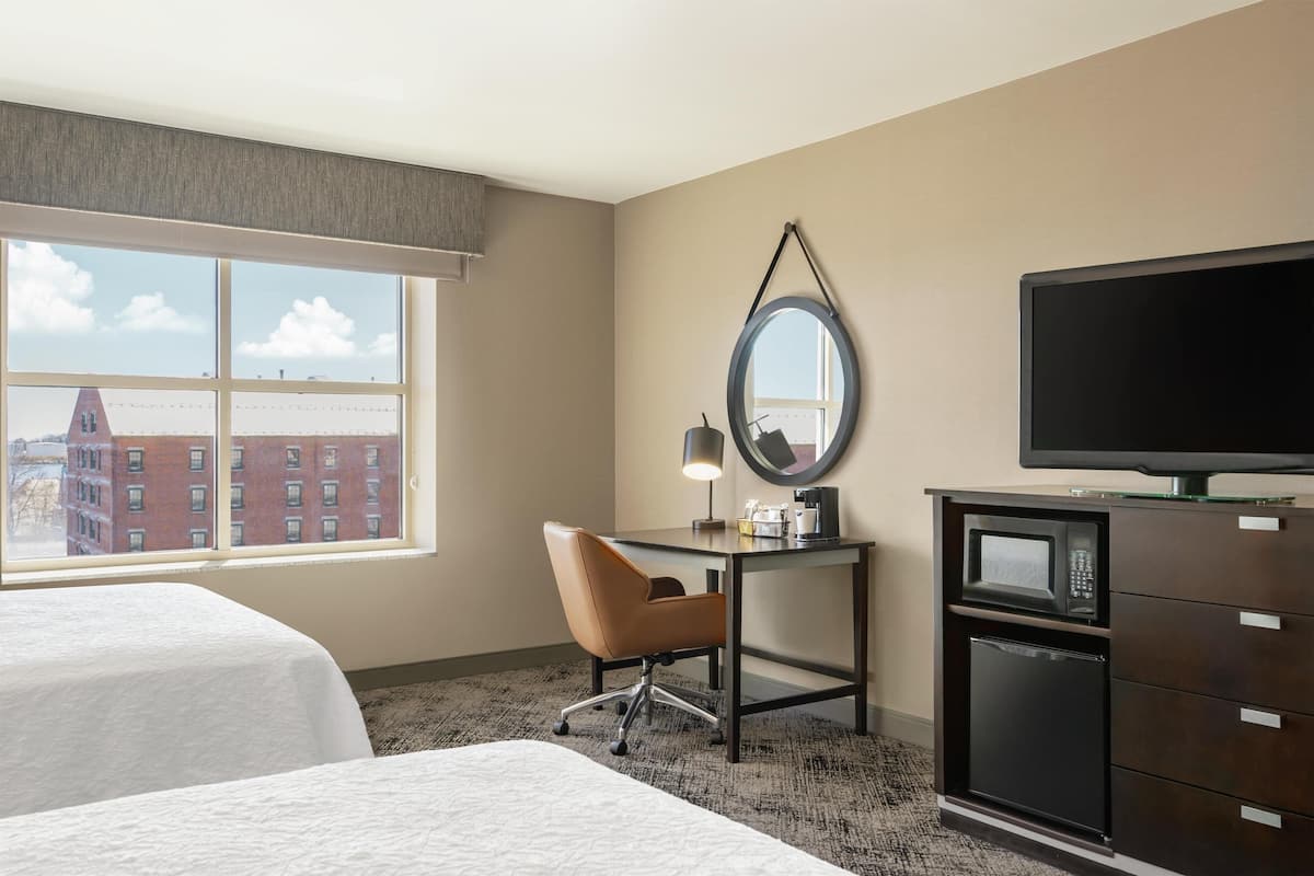 A hotel room with two beds, a desk with a chair, a television, a microwave, and a dresser.