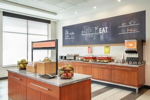 A modern kitchen with a chalkboard displaying food items, a juice dispenser, and a sign indicating breakfast availability.