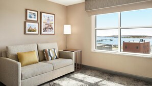A living room with a sofa, a small table, and a window with a view of a bridge and buildings.