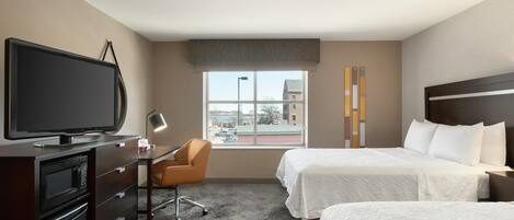 A hotel room with a TV, desk, chair, two beds, and a window with a city view.