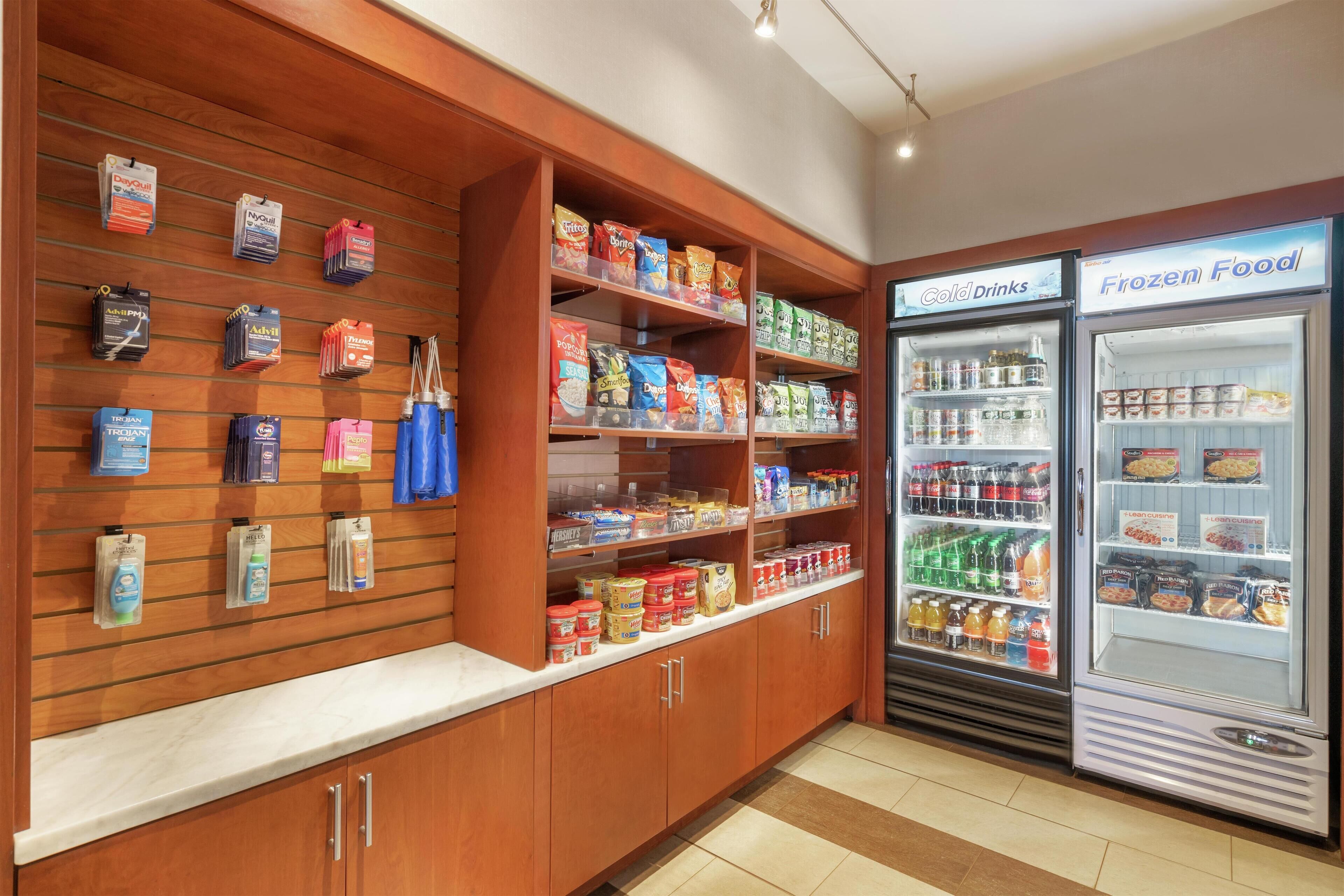 A grocery store with shelves stocked with snacks and beverages, and two refrigerated freezers labeled "Cold Drinks" and "Frozen Food".