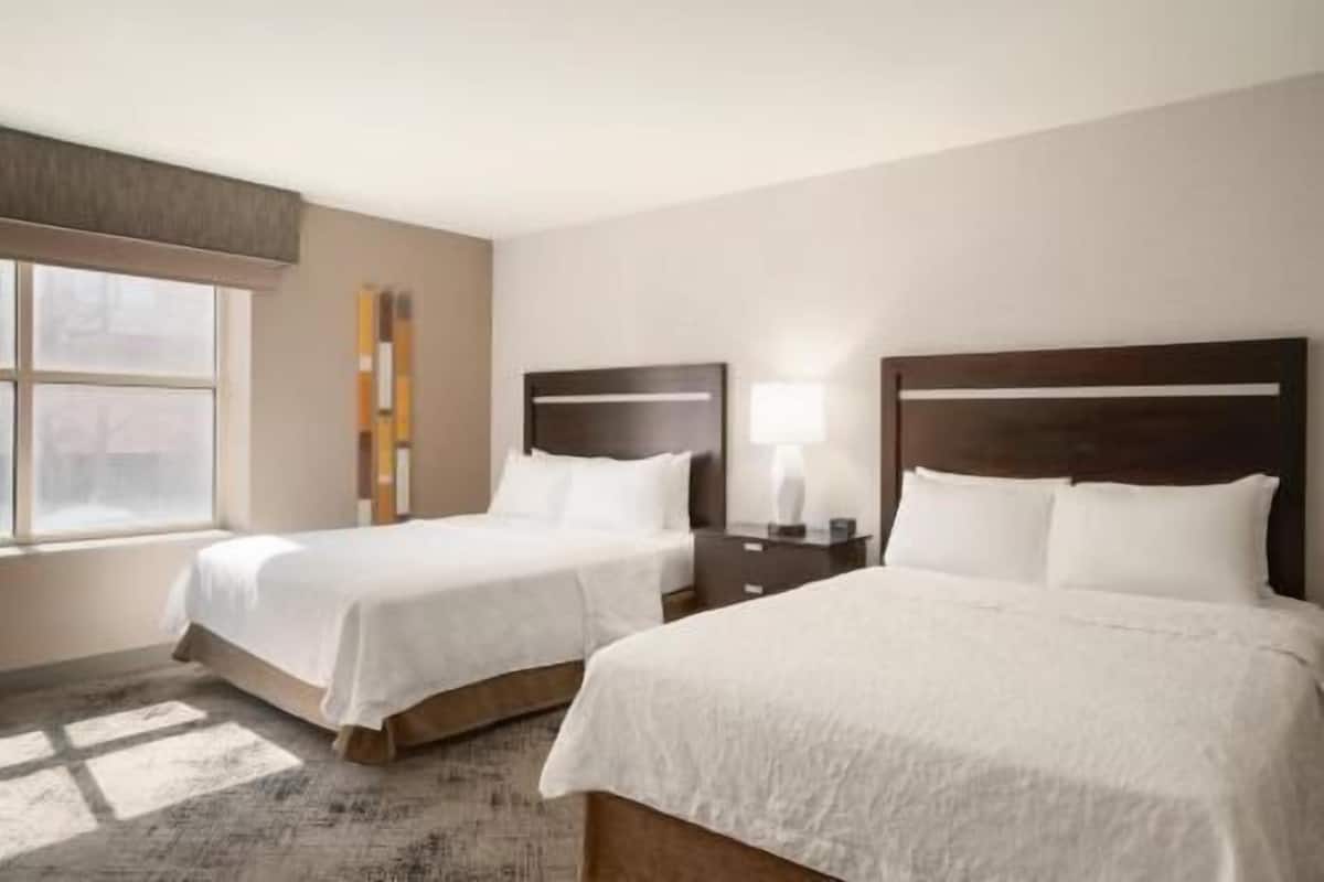 A hotel room with two beds, a window, a nightstand, and a lamp.
