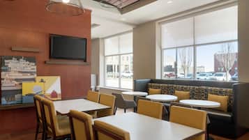 A modern dining area with tables and chairs, a large window with a view of the street, and a television mounted on the wall.
