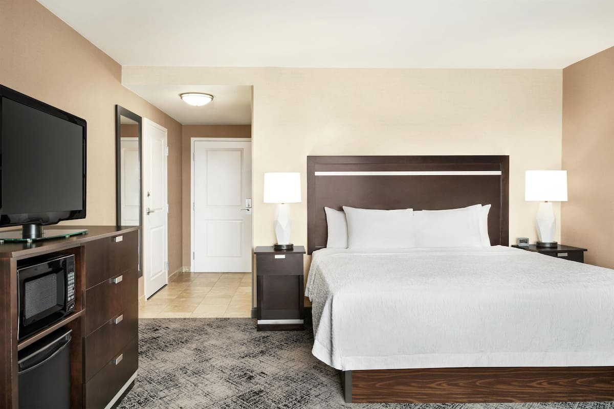 A hotel room with a bed, bedside tables with lamps, a TV on a cabinet, and a microwave.