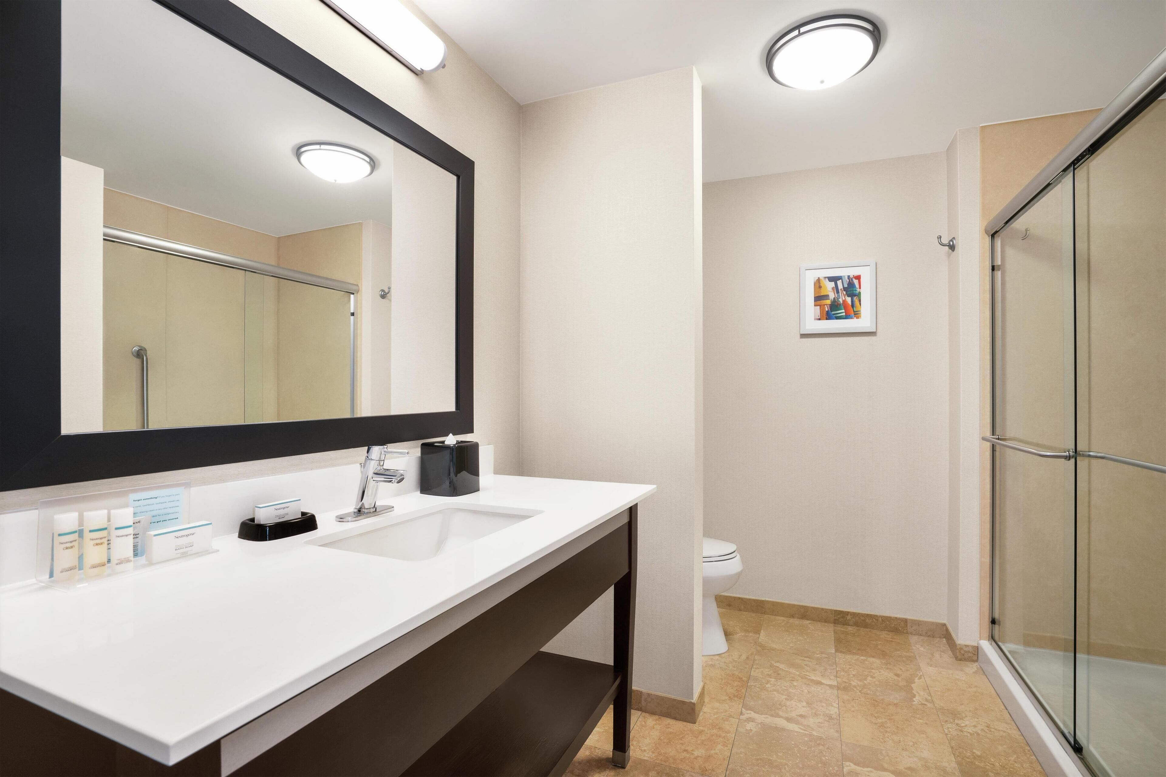 Un baño con lavabo blanco, un espejo grande y cabina de ducha de cristal.