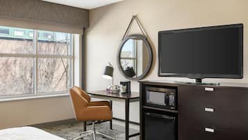 Habitación de hotel con cama, escritorio con silla, televisor, espejo y minibar.
