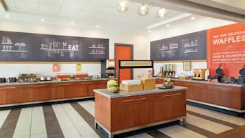 Cozinha moderna com ilha central, diversos eletrodomésticos e parede de quadro negro com desenhos de comida.