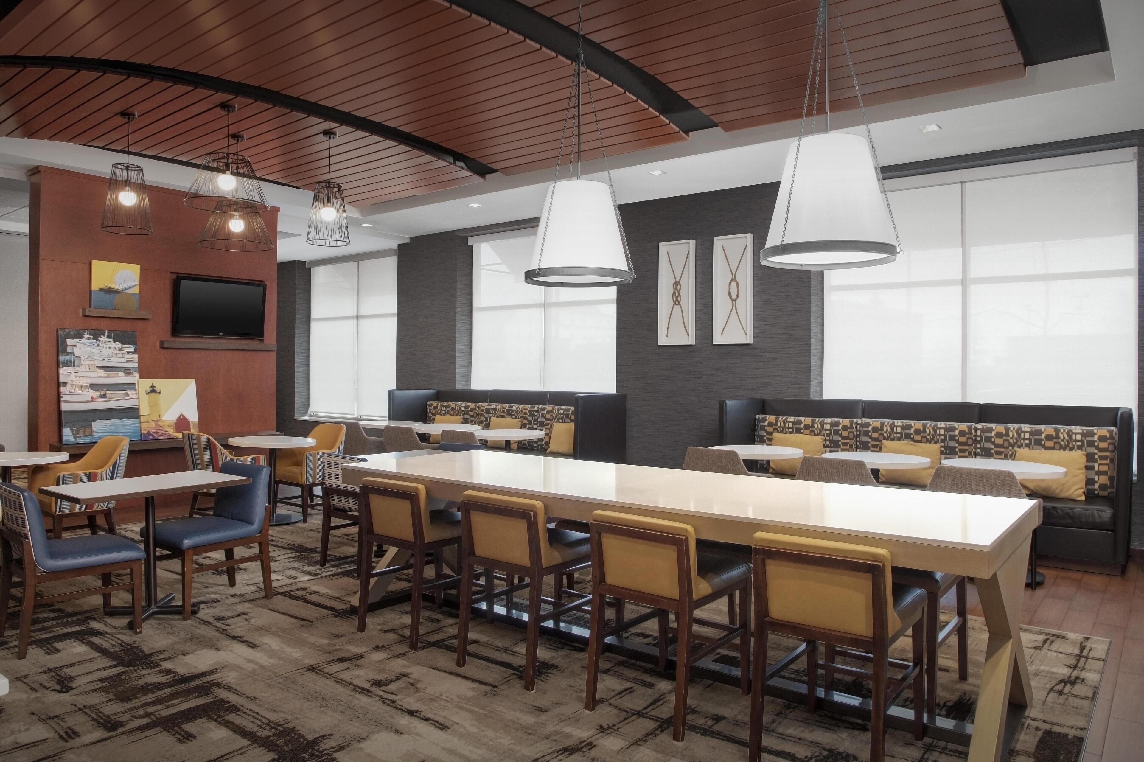 Un espace de restauration moderne doté d’une longue table conviviale, de plusieurs options d’assises et d’un éclairage suspendu.