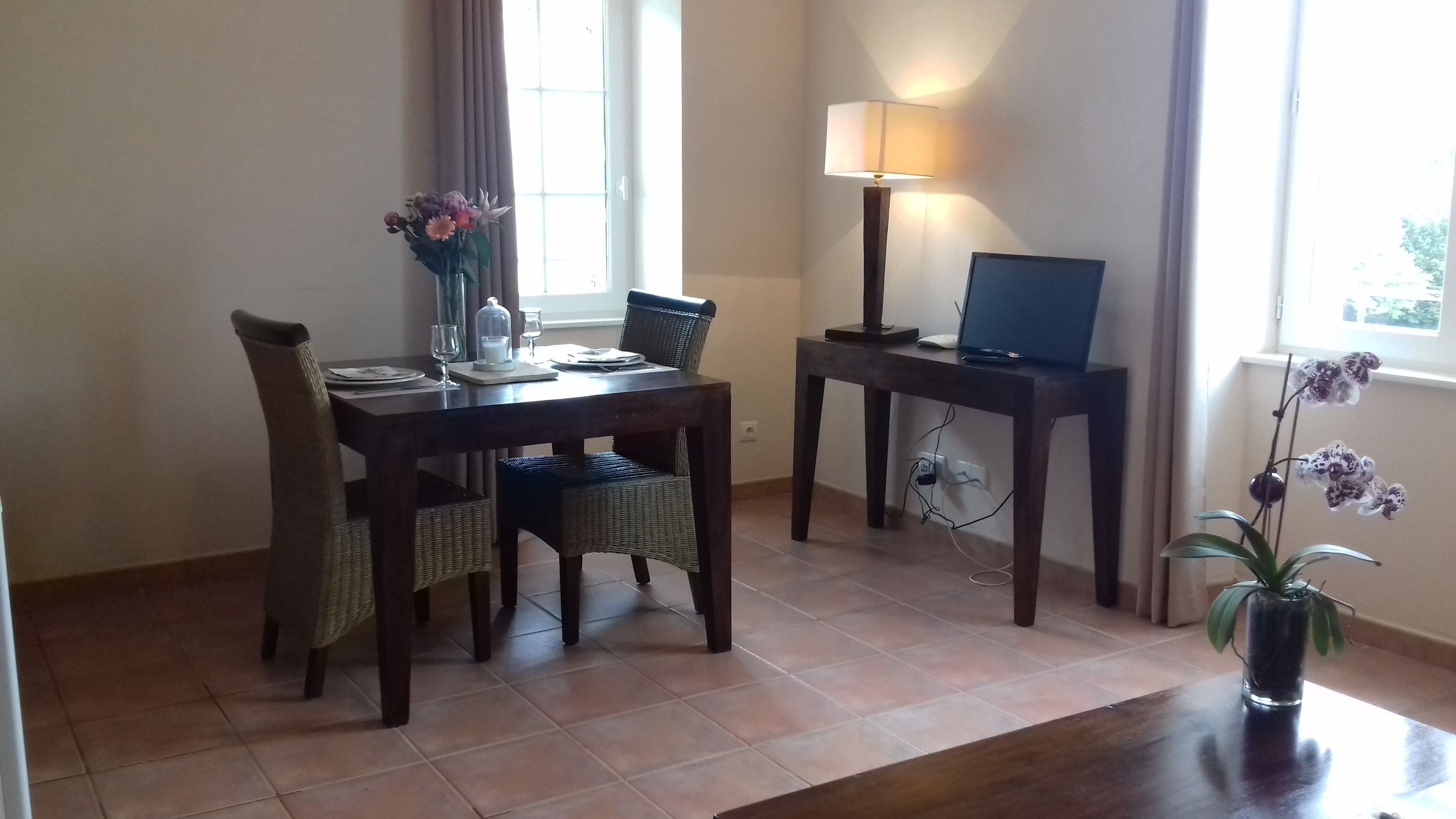 Un coin repas avec une table dressée pour deux personnes, une lampe, un ordinateur portable et une orchidée en pot.