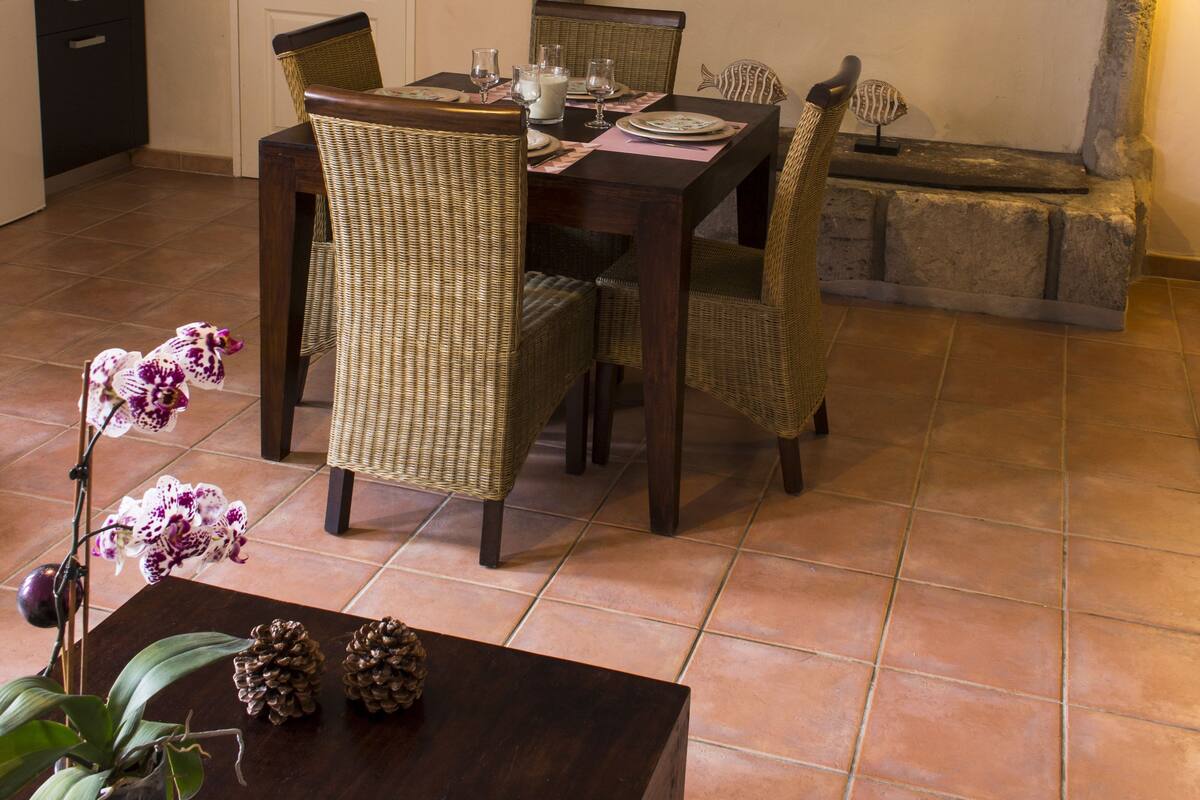 Un coin repas agrémenté d’une cheminée en pierre, de chaises en osier et d’une table dressée pour quatre personnes.
