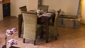 Een eetgedeelte met een stenen openhaard, rieten stoelen en een tafel gedekt voor vier personen.