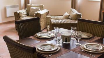 Une table à manger dressée pour quatre personnes, avec des chaises en osier, un centre de table composé de bougies et, en arrière-plan, un canapé en osier.