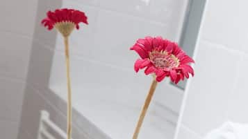 Un baño con un lavamanos blanco, un florero con una flor rosa y dos botellas de aceite de argán.