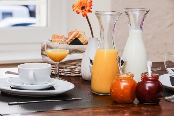 A breakfast setting with a cup, a glass of orange juice, a pitcher of milk, and two jars of jam.