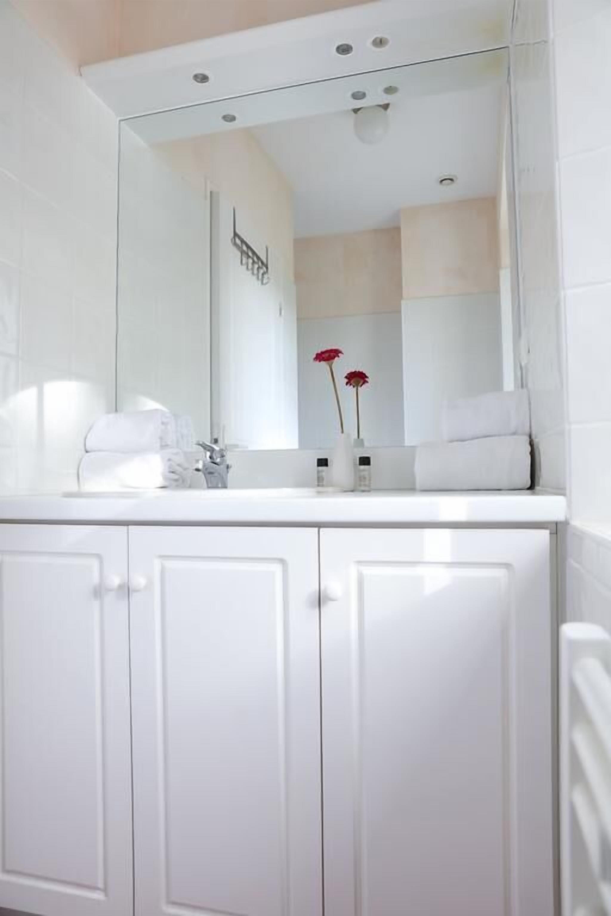 A modern bathroom with a white vanity, a large mirror, and a towel rack.
