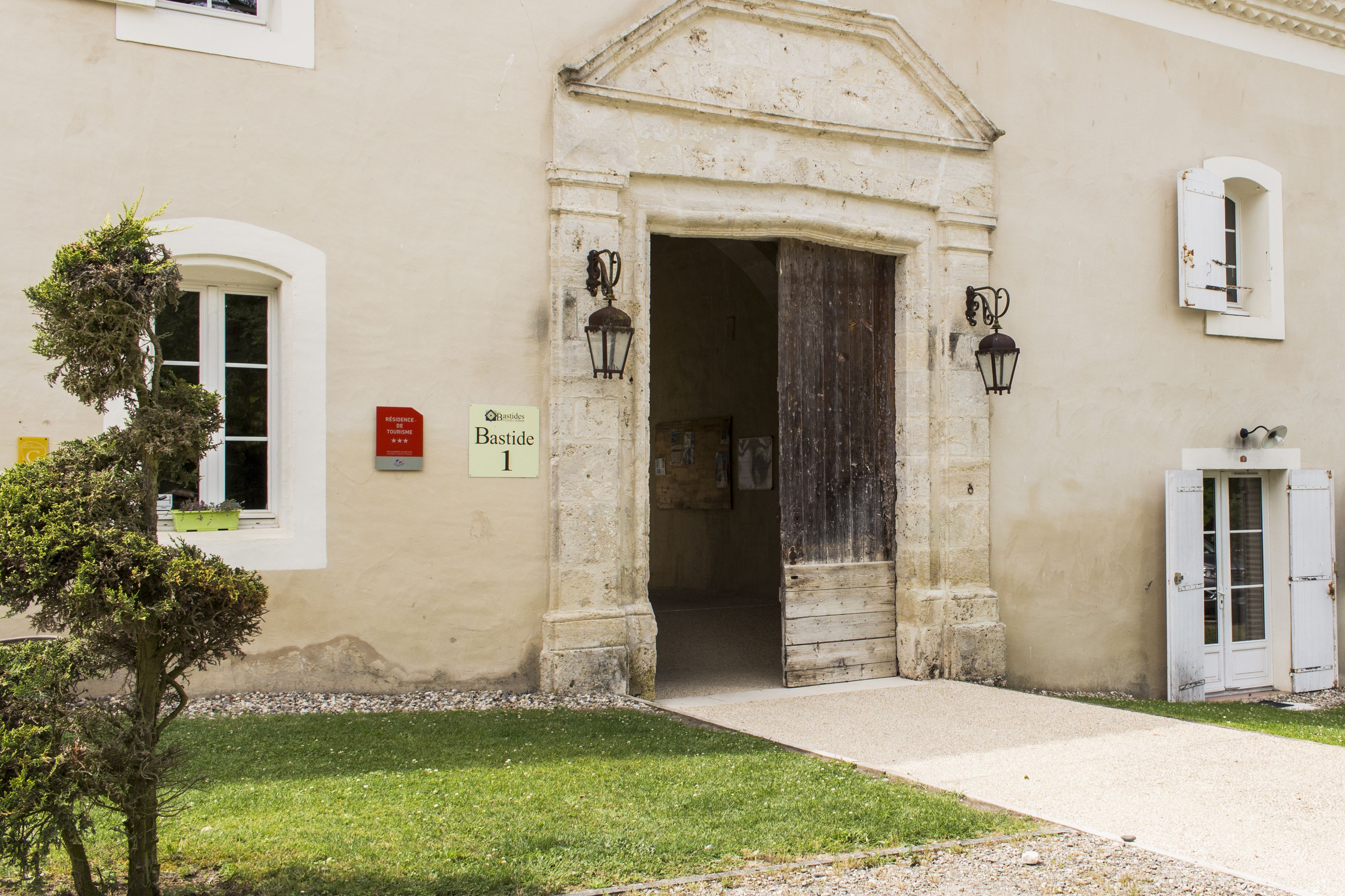 Entrada de un edificio con un arco de piedra, un cartel que indica residencia turística y un pequeño árbol en primer plano.
