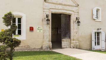 Entrada de un edificio con un arco de piedra, un cartel que indica residencia turística y un pequeño árbol en primer plano.