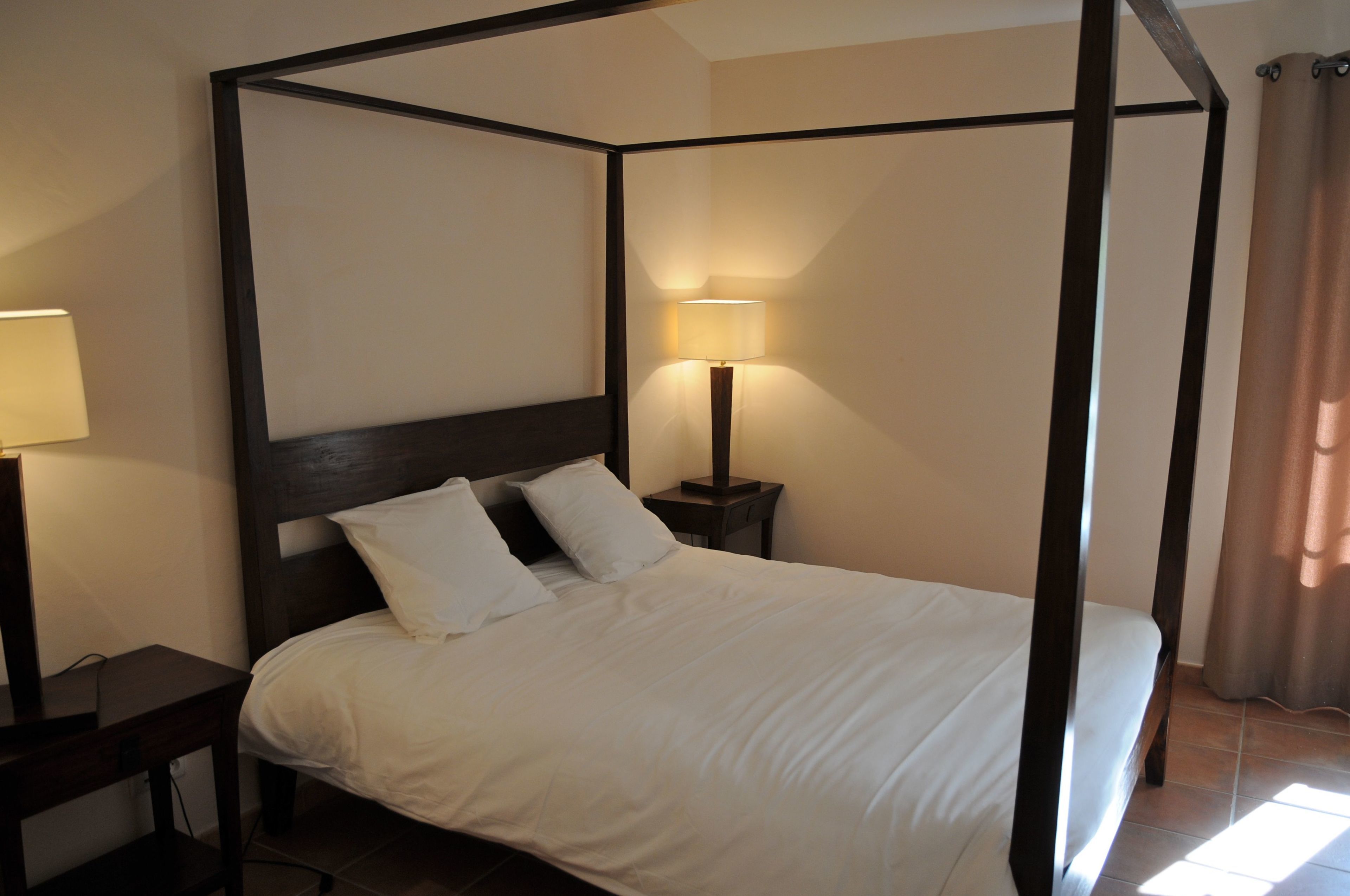 A four-poster bed with white linens, a bedside lamp, and a nightstand.