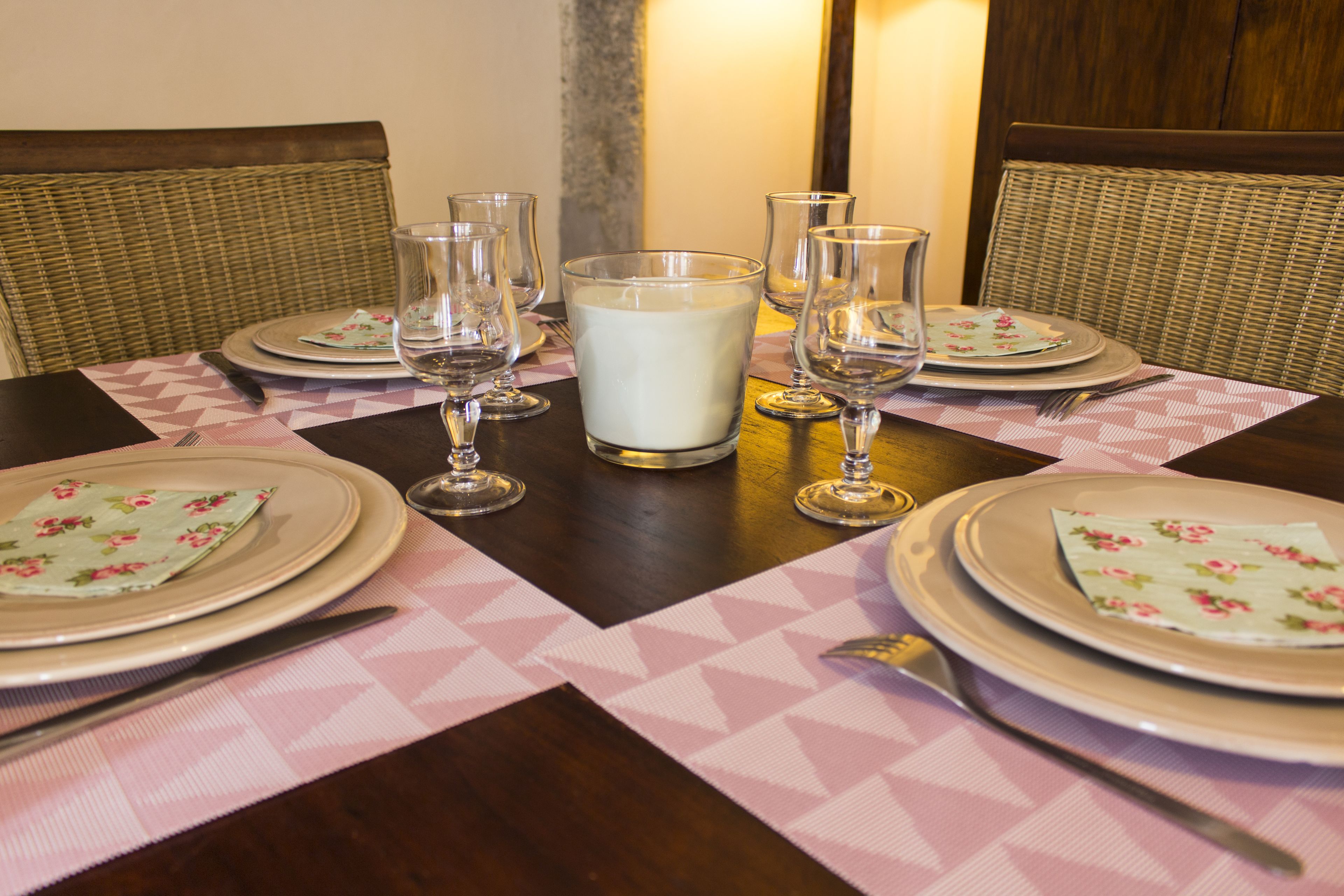 Een eettafel gedekt met borden, glazen en bestek, omringd door rieten stoelen.