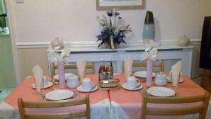 A dining table set for four with white plates, cups, and a centerpiece of flowers. - Priory Guest House (Cleethorpes)