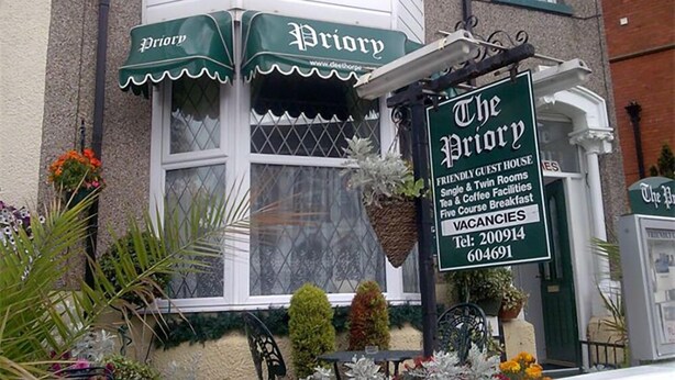 A corner building with a green awning labeled "Priory" and a signboard stating "The Priory" with amenities like guest house, rooms, tea, coffee, and breakfast. - Priory Guest House (Cleethorpes)