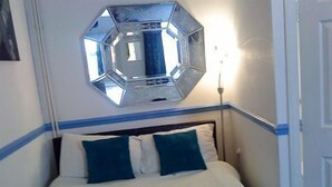 A bed with a headboard, a wall-mounted mirror, and a bedside lamp. - Priory Guest House (Cleethorpes)