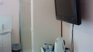 A bathroom with a sink, mirror, and a television mounted on the wall. - Priory Guest House (Cleethorpes)