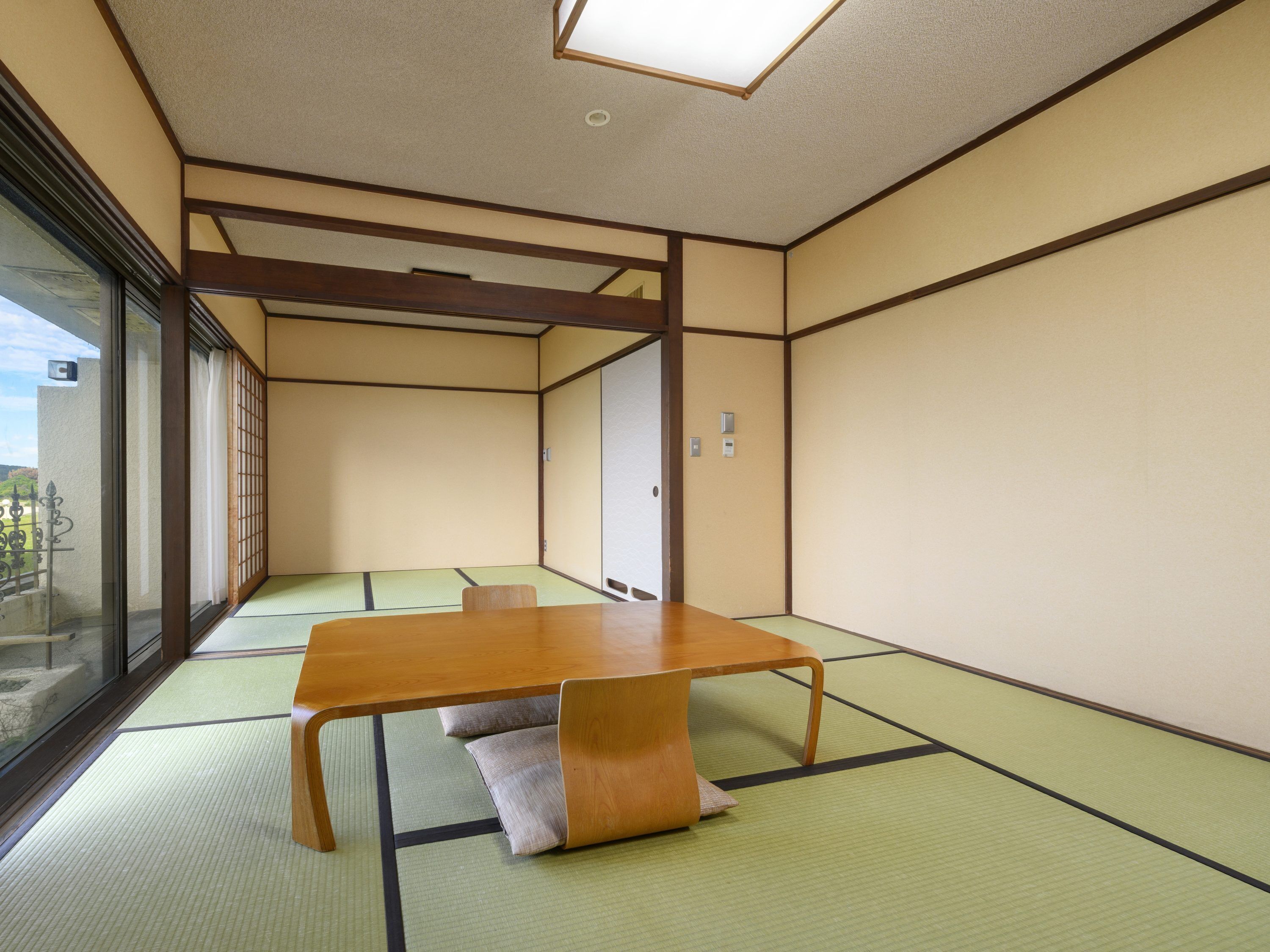Una habitación tradicional de tatami con una mesa baja, cojines, ventanas amplias y puertas correderas.