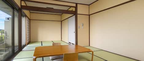 Una habitación tradicional de tatami con una mesa baja, cojines, ventanas amplias y puertas correderas.