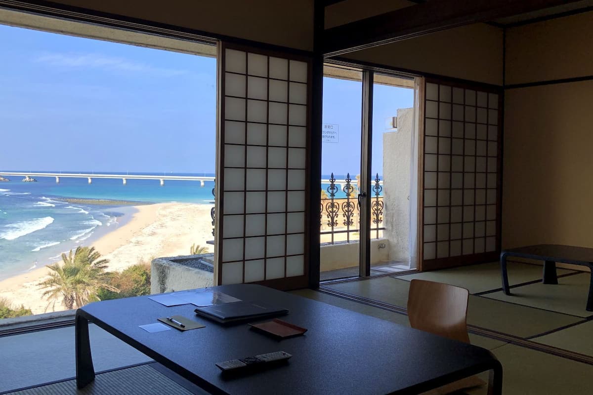 Una habitación con suelo de tatami, una mesa con material de escritura y vistas a la playa y al océano.