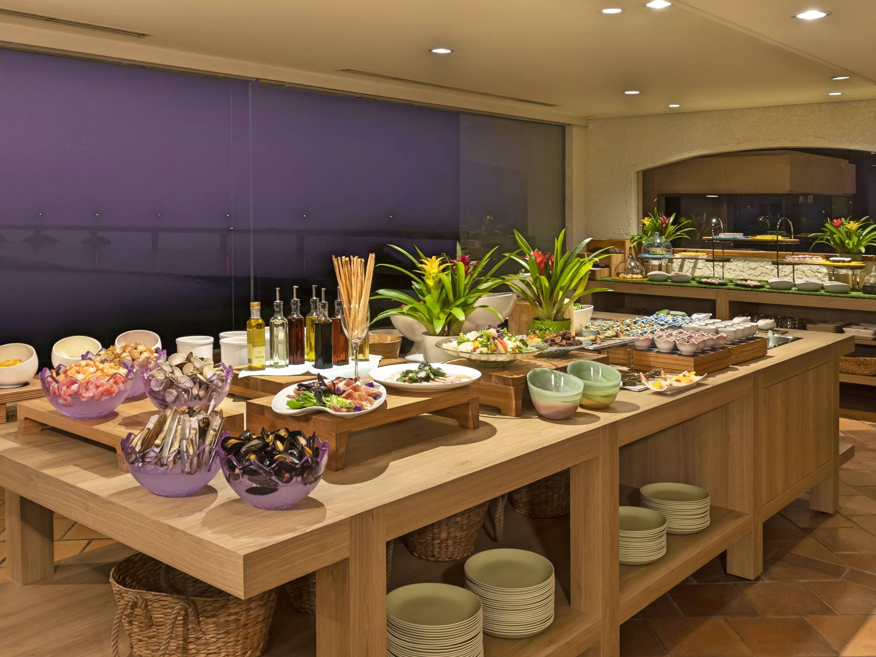 A buffet setup with various food items, including seafood, salads, and beverages, arranged on a wooden table with a purple backdrop.