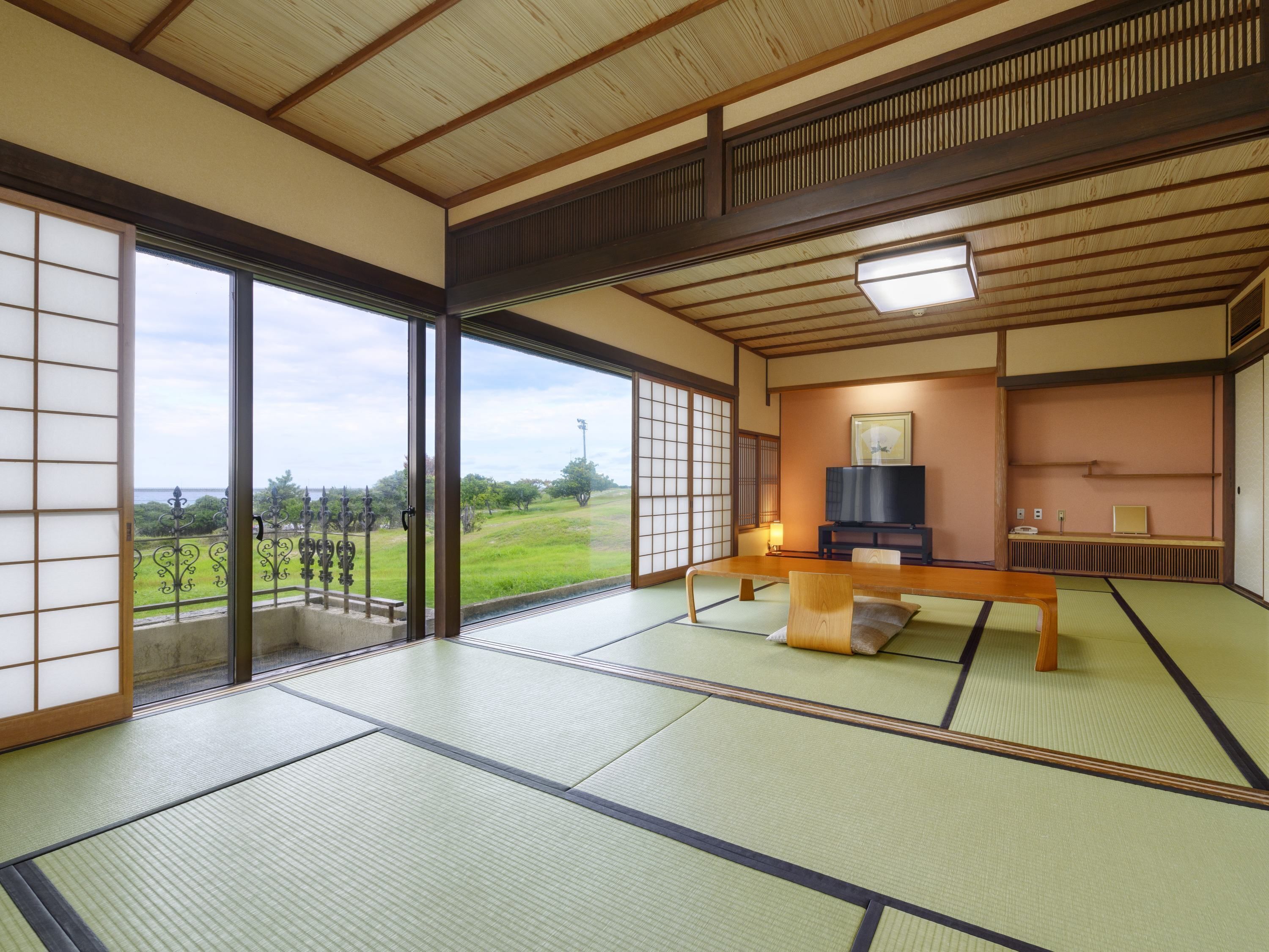 A traditional Japanese room with tatami flooring, a low table, a television, and a view of a green landscape.