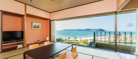 Een kamer met een grote tafel, tatami matten, een televisie en uitzicht op zee.